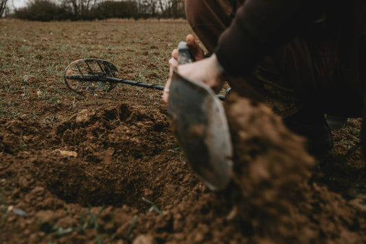 metal detector lying on the ground and a person digging with a shovel