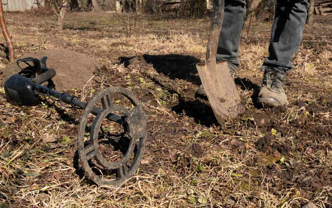 metal detector lying on the ground and a man standing holding a shovel