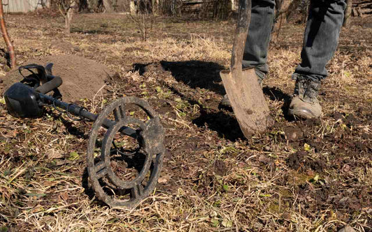 metal detector lying on the ground and a man standing holding a shovel