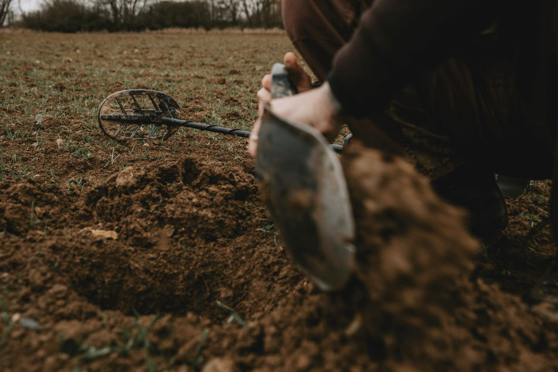 metal detector lying on the ground and a person digging with a shovel