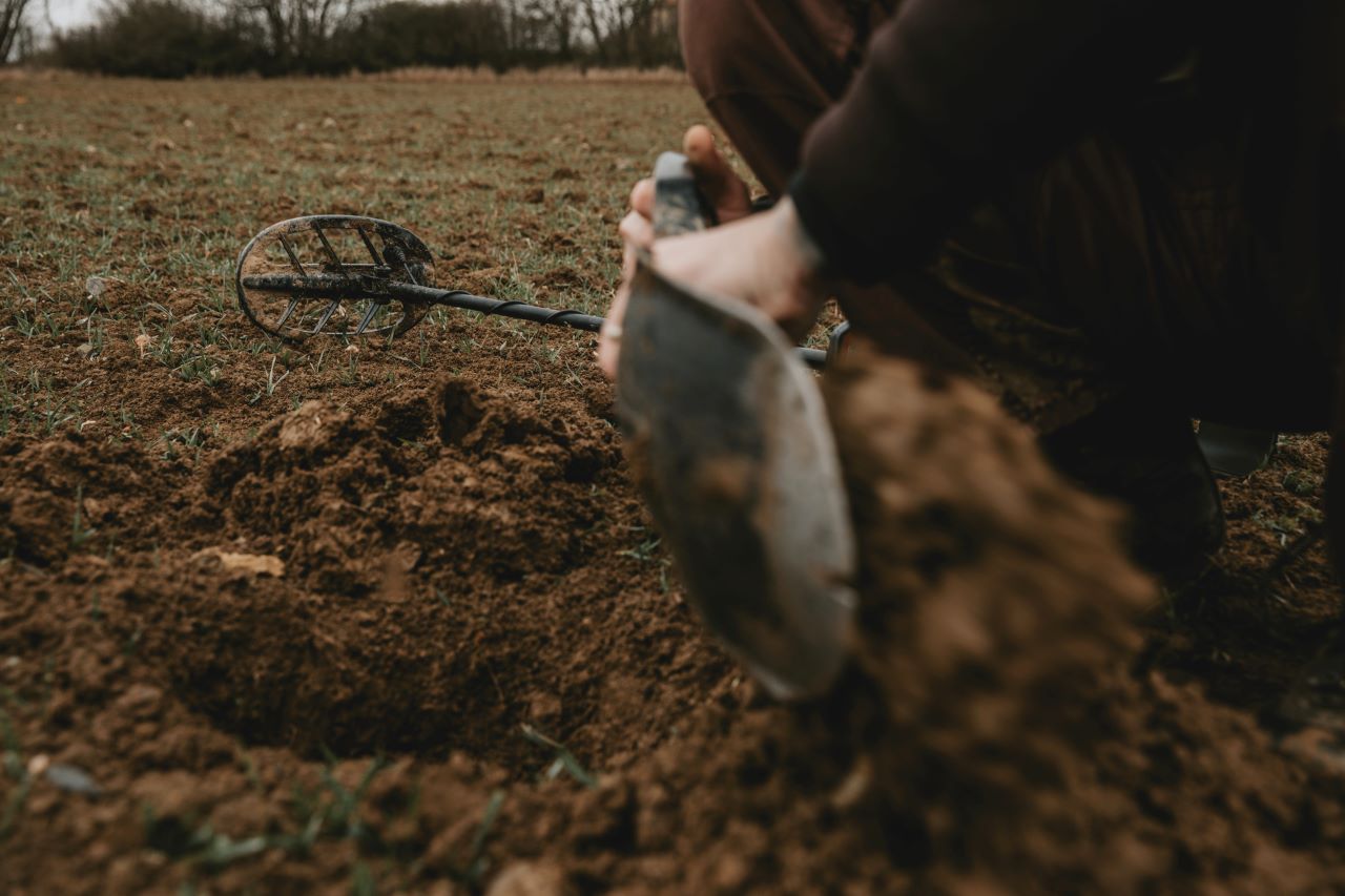metal detector lying on the ground and a person digging with a shovel