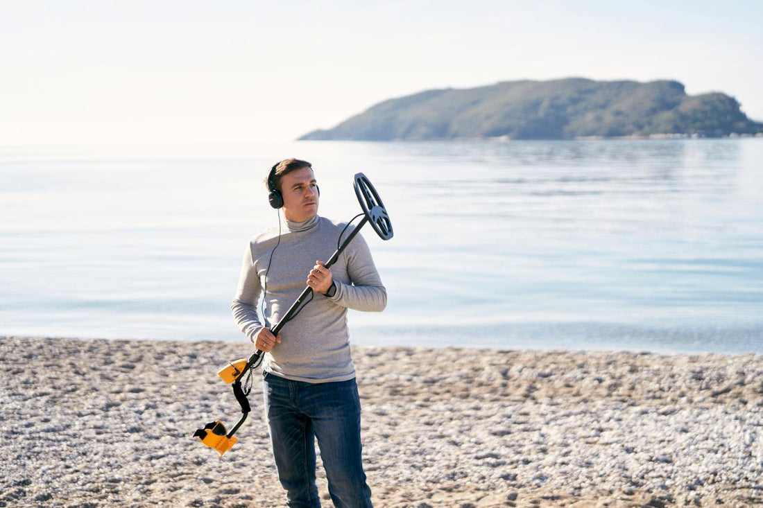 man holding and looking at a metal detector on a beach