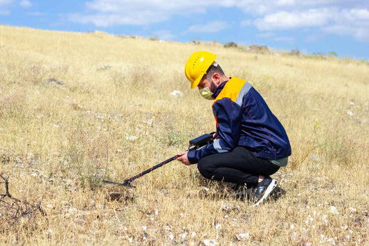 man squatting down holding a metal detector